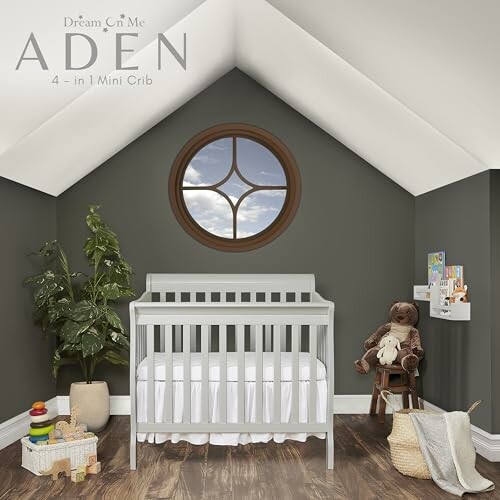 White mini crib in a cozy nursery with toys and plants.