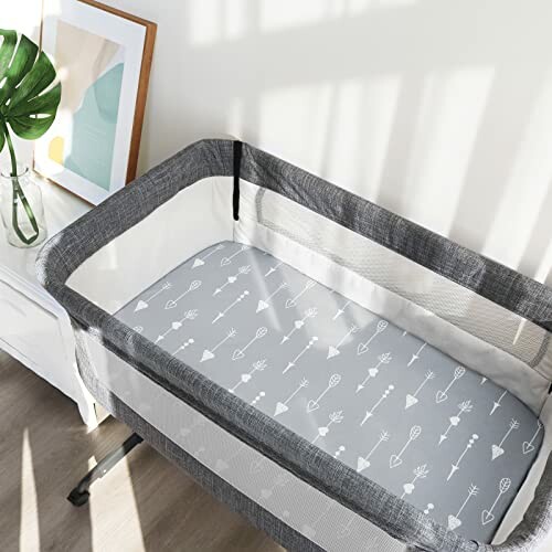 A baby bassinet with grey bedding featuring arrow patterns.