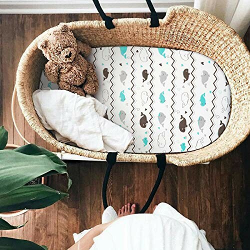 Baby bassinet with teddy bear and patterned sheet.