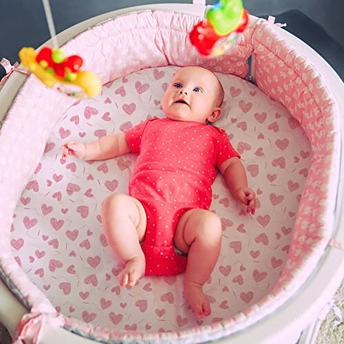 Baby in pink playpen with hanging toys.