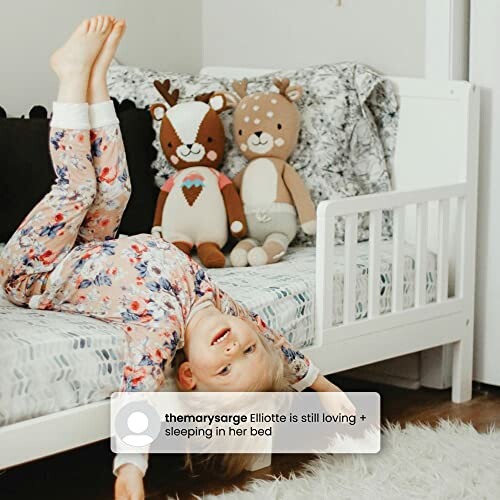 Child in pajamas playfully lying on a bed with deer stuffed animals.