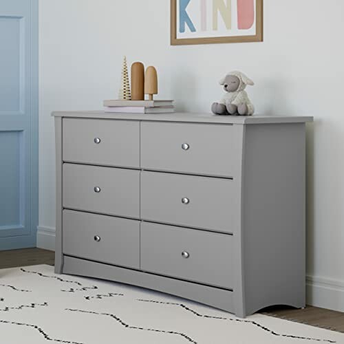 Gray dresser with six drawers and decorations on top in a nursery room.