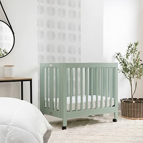 Mint green baby crib in a nursery with leaf-patterned wallpaper.