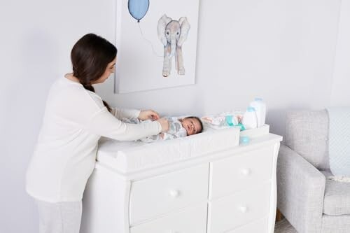 Mother changing baby's diaper on changing table in nursery.