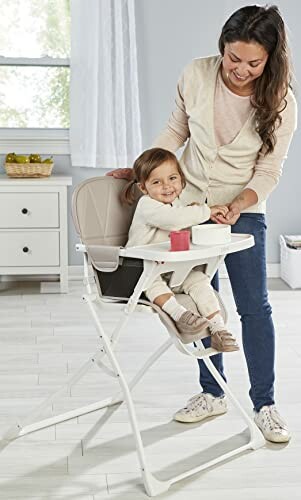 Mother feeding toddler in a high chair indoors.