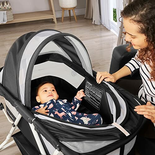 Mother smiling at baby lying in a black and white bassinet indoors.