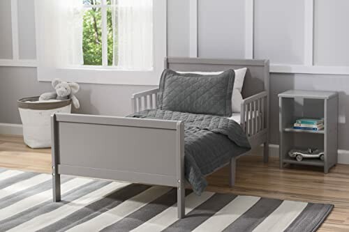 Gray toddler bed with bedding in a bright room.