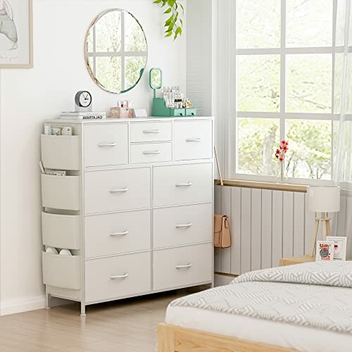 White dresser with multiple drawers and a round mirror in a bright bedroom.